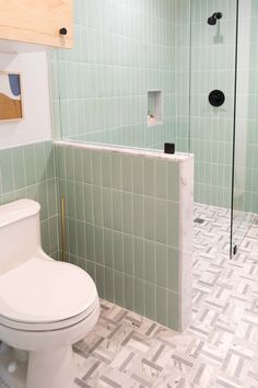 a white toilet sitting inside of a bathroom next to a walk in shower and tiled floor