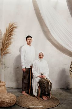 two people standing next to each other in front of a wall with white drapes