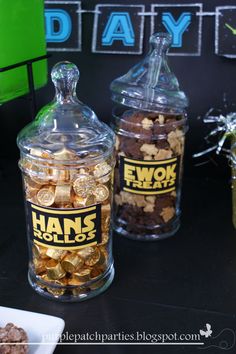 two glass jars filled with gold coins on top of a black table next to a white plate