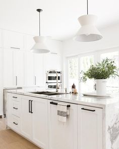 a kitchen with white cabinets and an island in front of a window that has plants on it