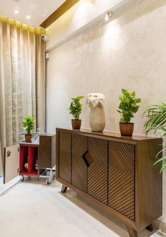 two potted plants on top of a wooden cabinet in a room with white walls