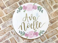 a wooden sign that says ava noele with pink flowers and green leaves on it