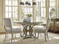 a dining room table with four chairs and a vase on the table in front of two windows