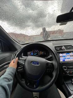 a person driving a car in the rain with their hands on the steering wheel and dashboard