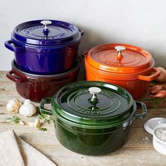 three different colored pots sitting on top of a wooden table next to garlic and onions