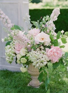 a vase filled with pink and white flowers on top of a lush green field next to a statue