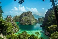 the water is crystal blue and green with small boats in it, surrounded by trees