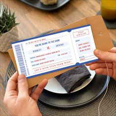 a person holding up a ticket for a game in front of a table with plates and cups