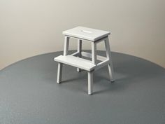 a small white step stool sitting on top of a gray table next to a wall