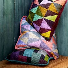 two multicolored pillows sitting on top of a wooden table next to a green wall