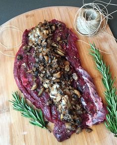 a piece of meat sitting on top of a wooden cutting board next to sprigs of rosemary