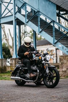 a man riding on the back of a motorcycle down a street next to a blue bridge