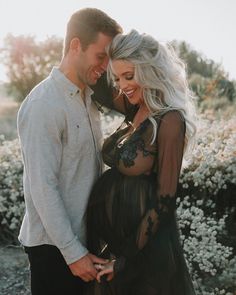 a man and woman standing next to each other in front of some bushes with white flowers