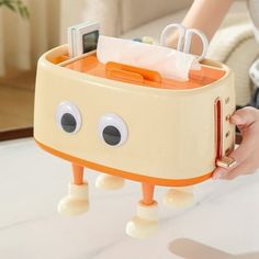 an orange and white toaster with eyes on it's side holding a tissue dispenser