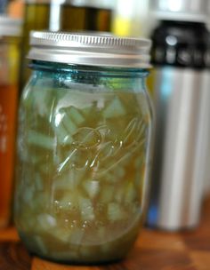 a jar filled with pickles sitting on top of a wooden table next to other jars