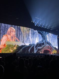 a large screen with a woman on it in front of a crowd