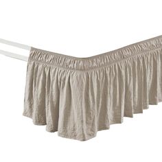 a tan ruffled bed skirt hanging on a clothes line with two white rails in front of it