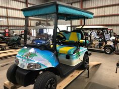 a golf cart painted with tropical scenes is parked in a garage next to other vehicles