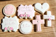 decorated cookies with pink and white frosting are arranged on a wooden table next to a crucifix