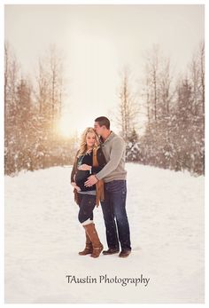 a man and woman standing in the snow with their arms around each other as they cuddle