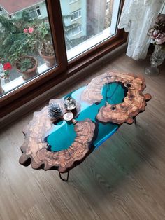 a coffee table made out of wood and blue glass in front of a window with potted plants on it