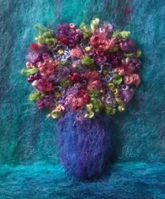 a blue vase filled with lots of flowers on top of a table next to a green wall