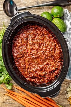 a crock pot filled with chili and carrots on top of a wooden table