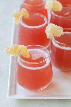 four glasses filled with red liquid and garnished with orange peels on a white plate