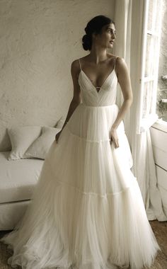 a woman standing in front of a window wearing a white dress