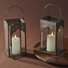 two lit candles are sitting on a wooden table next to a metal holder with a candle in it