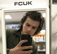 a man looking at his cell phone while standing in front of a vending machine