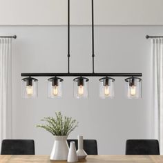 a dining room table with four lights hanging from it's center and two vases on the other side