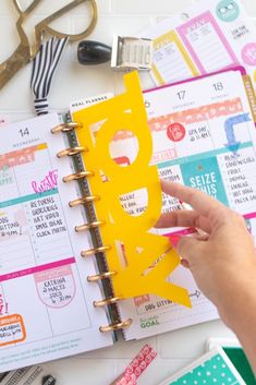 a person holding a planner in their hand next to some scissors and other office supplies