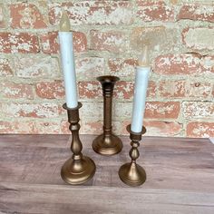 two brass candlesticks sitting on top of a wooden table next to a brick wall