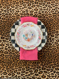 an empty plate sitting on top of a cheetah print table cloth next to a pink napkin