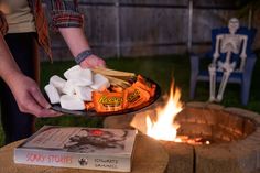 a person holding marshmallows over a fire pit with a book on it