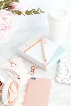 an iphone and headphones on a desk next to a keyboard, phone case, flower vase with pink peonies