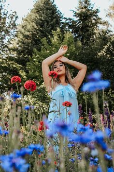 a woman in a blue dress standing in a field of flowers with her hands behind her head