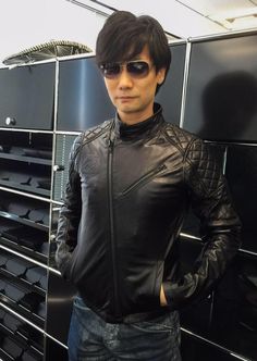 a man in black leather jacket and sunglasses standing next to some metal racks with glasses on them