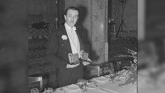 an old photo of a man standing in front of a table