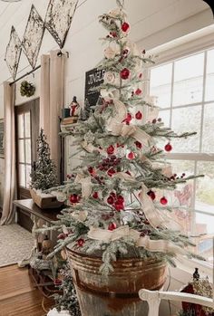 a white christmas tree with red and silver ornaments in a pot on the floor next to a window