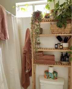 a bathroom with plants and towels on the shelf next to the toilet, along with a shower curtain