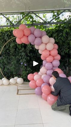 a man kneeling down next to a giant letter made out of pink and white balloons