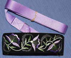 a purple ribbon with flowers and leaves on it next to a lanyard or key fobl