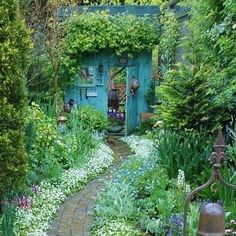 a garden with lots of flowers and plants around it, including an old blue door