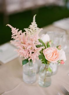 two vases filled with flowers sitting on top of a white tablecloth covered table