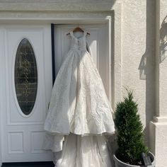 a wedding dress hanging on the front door of a white house with potted plants