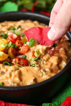 a hand dipping a tortilla chip into a bowl of dip