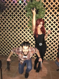 a man and woman posing for a photo in front of a fence with plants on it