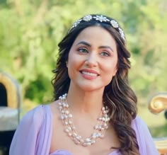 a woman in a purple dress is smiling at the camera and wearing a pearl necklace